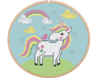 Puede incluir: Un unicornio blanco con una crin y cola de arcoíris se encuentra en un campo verde con un arcoíris en el cielo. Un pequeño pájaro rosa se sienta en la espalda del unicornio. La imagen es un patrón de punto de cruz.