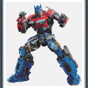Op de afbeelding: Een ingelijste kruissteek van Optimus Prime, een robotpersonage. De robot is voornamelijk blauw en rood, met zilveren en zwarte accenten. De afbeelding toont de robot in een dynamische pose, met opgeheven armen en gespreide benen.
