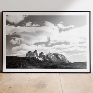 May include: Black and white photograph of a mountain range with a cloudy sky. The mountains are tall and jagged, and the sky is filled with fluffy clouds.