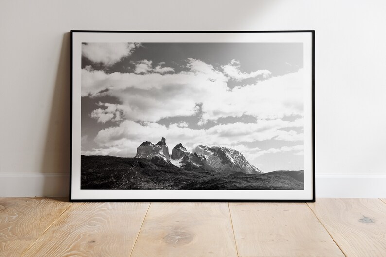 May include: Black and white photograph of a mountain range with a cloudy sky. The mountains are tall and jagged, and the sky is filled with fluffy clouds.