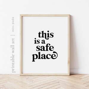 May include: A framed print with the text "this is a safe place" in a bold, retro font. The print is on a white background and is framed in a light wood frame.