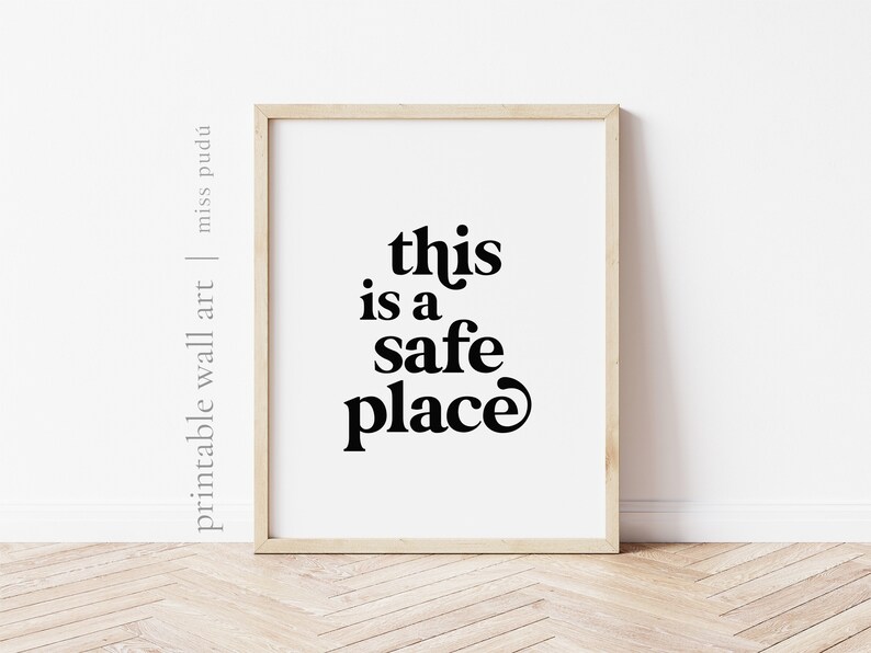 May include: A framed print with the text "this is a safe place" in a bold, retro font. The print is on a white background and is framed in a light wood frame.