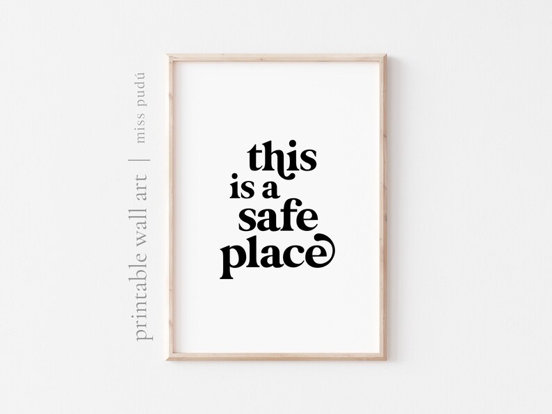 May include: A framed print with the text "this is a safe place" in a bold, retro font. The print is on a white background and is framed in a light wood frame.
