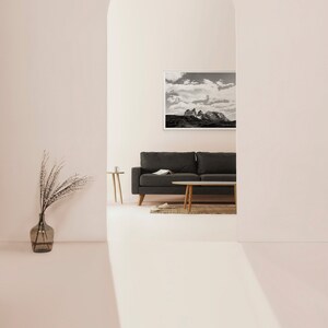 May include: A black sofa with a throw pillow sits in front of a black and white photograph of a mountain range. The sofa is in a room with a white archway and a light pink wall.