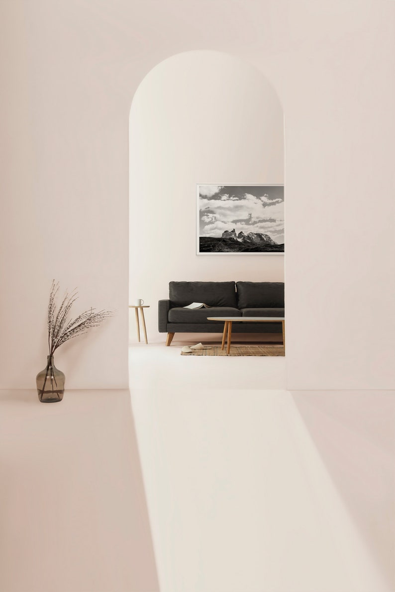 May include: A black sofa with a throw pillow sits in front of a black and white photograph of a mountain range. The sofa is in a room with a white archway and a light pink wall.