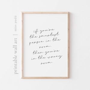 May include: A framed print with a minimalist design. The artwork features a quote in black script: "If you're the smartest person in the room, then you're in the wrong room." The frame is a light wood colour, and the background is white.