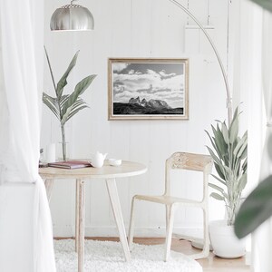 May include: A white round table with a white chair and a white rug. A black and white photo of a mountain range is hanging on the wall above the table. A potted plant is on the floor next to the chair.