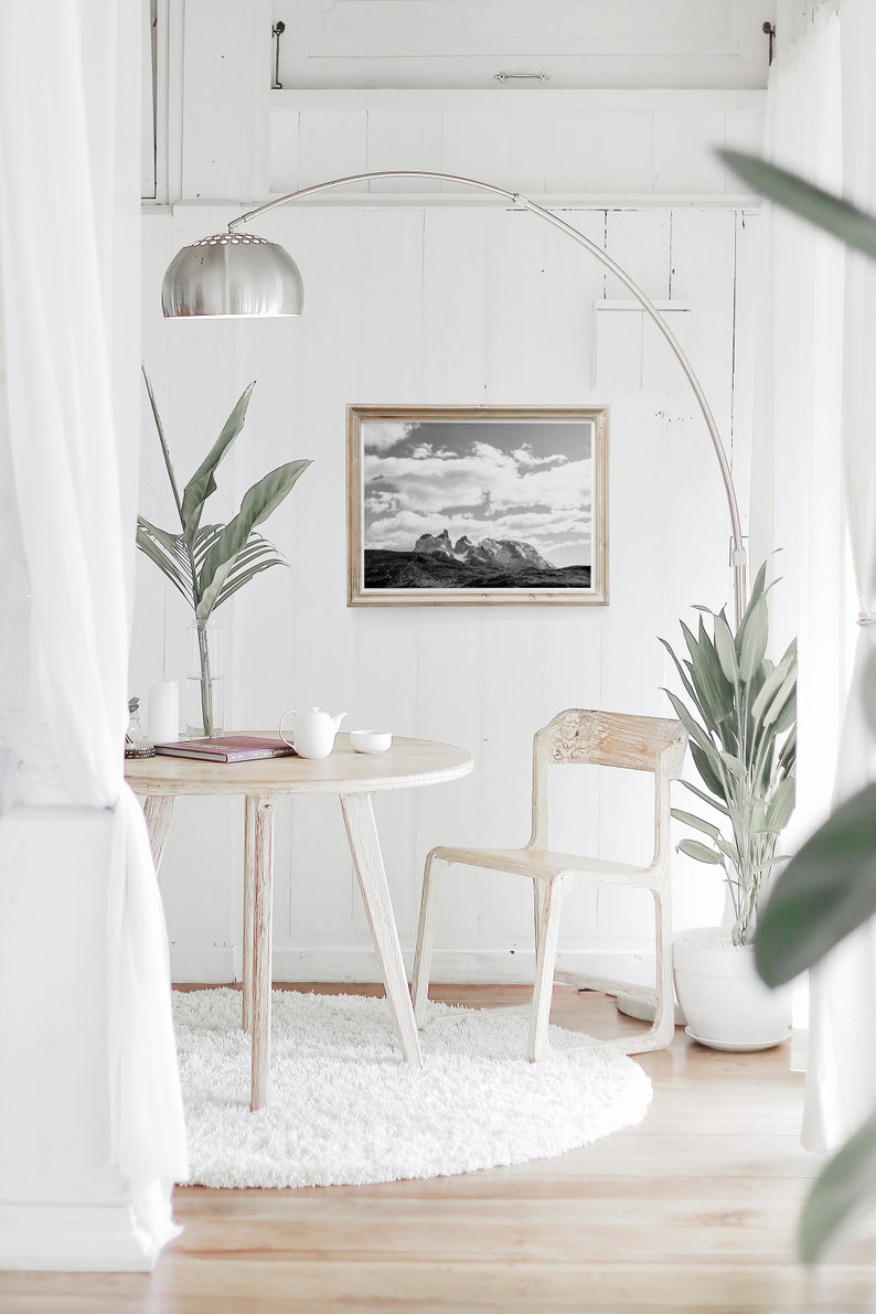 May include: A white round table with a white chair and a white rug. A black and white photo of a mountain range is hanging on the wall above the table. A potted plant is on the floor next to the chair.
