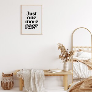 May include: A white wall with a framed print that reads "Just one more page". A wooden bench with a white throw blanket sits in front of the wall. A wicker basket sits on the floor next to the bench. A gold arched mirror and a bed with a white and brown blanket are in the background.