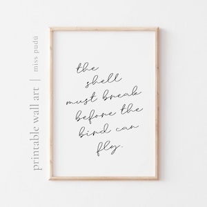 May include: A framed print with the quote "the shell must break before the bird can fly" in black script on a white background. The frame is a light wood color, and the words "printable wall art" and "miss pudú" are printed on the left side.
