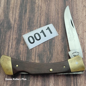 May include: A folding pocket knife with a wooden handle and brass accents. The blade is partially open, displaying the word "Frontier". A white sticker with the number "0011" is also visible.