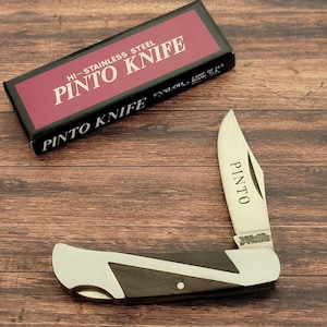 May include: A stainless steel Pinto Knife with a black and silver handle, and the word "Pinto" printed on the blade. The knife is open, and the box is visible with the words "Pinto Knife" printed on it.