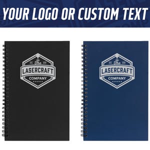 May include: Two spiral-bound notebooks, one black and one blue, are displayed. Each notebook features a white logo that reads "LASERCRAFT COMPANY" within a geometric design. The text "YOUR LOGO OR CUSTOM TEXT" is visible at the top.