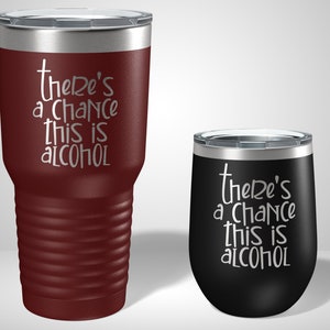 May include: Two stainless steel tumblers with a burgundy and black finish. The tumblers feature a white inscription that reads "there's a chance this is alcohol".