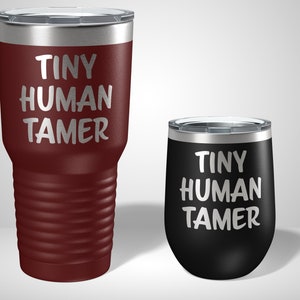 May include: Two stainless steel tumblers with the text "Tiny Human Tamer" on them. The larger tumbler is maroon and the smaller tumbler is black.