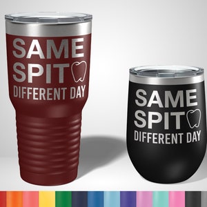 May include: Two insulated tumblers, one burgundy and one black, with silver text. The text on both reads "SAME SPIT DIFFERENT DAY" with a tooth graphic. The burgundy tumbler is cylindrical with a ridged design, and the black tumbler is a stemless wine glass shape.