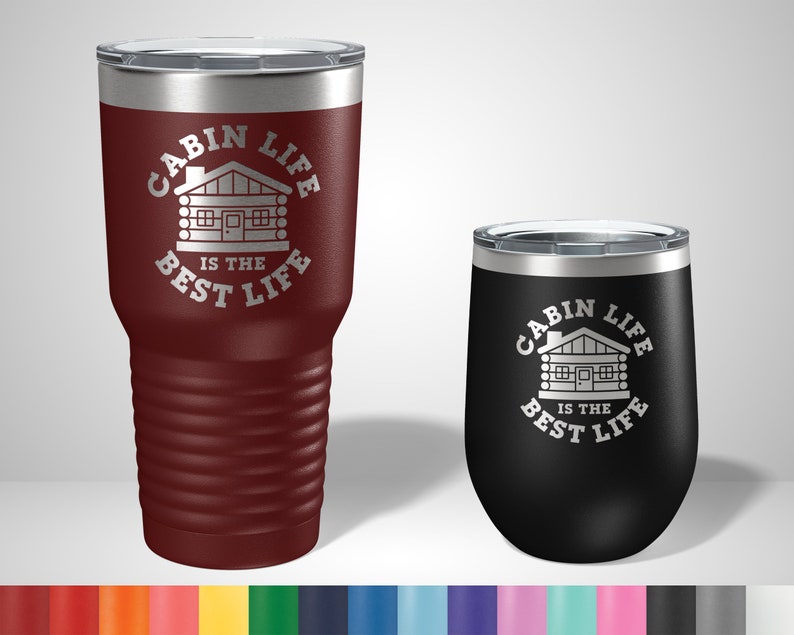 May include: Two stainless steel tumblers with a cabin life design. The larger tumbler is maroon and the smaller tumbler is black. Both tumblers have a white cabin graphic and the text "Cabin Life is the Best Life".