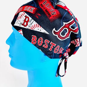 May include: A navy blue surgical scrub cap featuring the Boston Red Sox logo and team name in red and white. The cap includes the words "SOX" and "BOSTON RED SOX" in a repeating pattern. The cap is tied at the back.