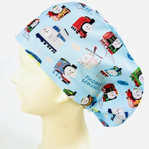 May include: A light blue scrub cap with a repeating pattern of cartoon trains and the text "THOMAS & FRIENDS". The cap is made of a soft fabric and is designed to cover the head and hair.
