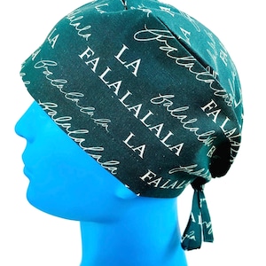 May include: A dark teal scrub cap with white script that reads "Fa La La La La". The cap is tied in the back with two small fabric ties. The cap is on a blue mannequin head.