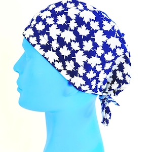 May include: A scrub cap featuring a vibrant royal blue background adorned with a repeating pattern of crisp white maple leaves. The head covering is designed with a tie-back closure at the nape of the neck, ensuring a secure and adjustable fit.