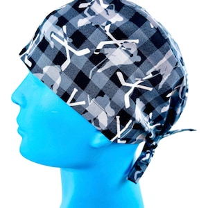 May include: A black and white patterned surgical scrub hat with a tie. The pattern features a camouflage design with hockey sticks and players.