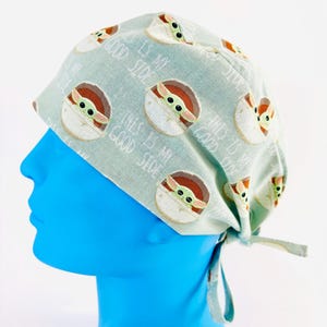 May include: A light green surgical scrub hat with a repeating pattern of a cartoon character with the text "This is my good side" on it.