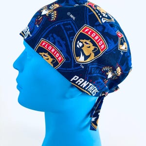 May include: A navy blue scrub cap featuring the Florida Panthers logo and team name. The cap has a repeating pattern of the team logo, with the words "FLORIDA" and "PANTHERS" visible. The cap is tied at the back.