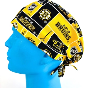 May include: A yellow, black, and white Boston Bruins scrub cap. The cap features the team's logo, the NHL logo, and the words "Boston Bruins". The cap is tied at the back.