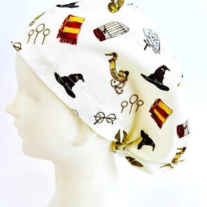 May include: White fabric cap featuring a repeating pattern of iconic wizarding world symbols. The design includes a red and gold scarf, a black wizard hat, golden snitch, and other themed illustrations. The cap is designed to be worn on the head.