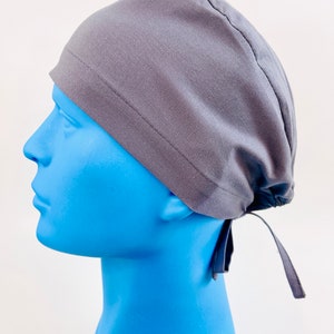May include: A grey scrub hat with a tie at the back. The hat is made of a soft, breathable fabric and is designed to be comfortable to wear for long periods of time.