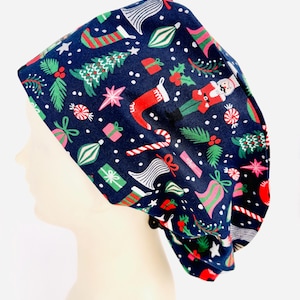 May include: A navy blue scrub cap featuring a Christmas-themed pattern. The design includes Christmas trees, stockings, gifts, candy canes, and ornaments in red, green, pink, and white. The cap is made of a soft, flexible fabric.