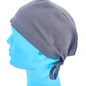 May include: A dark grey surgical scrub cap with a tie closure. The cap is made of a soft fabric and is designed to cover the head and hair. The cap is shown on a blue mannequin head against a white background.