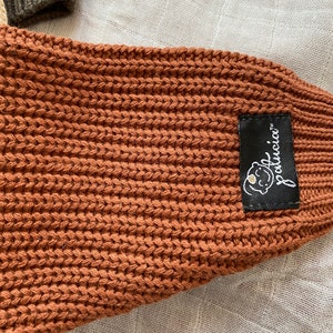 May include: A brown knitted baby blanket with a black label that says "LouLouci" with a small white flower graphic.