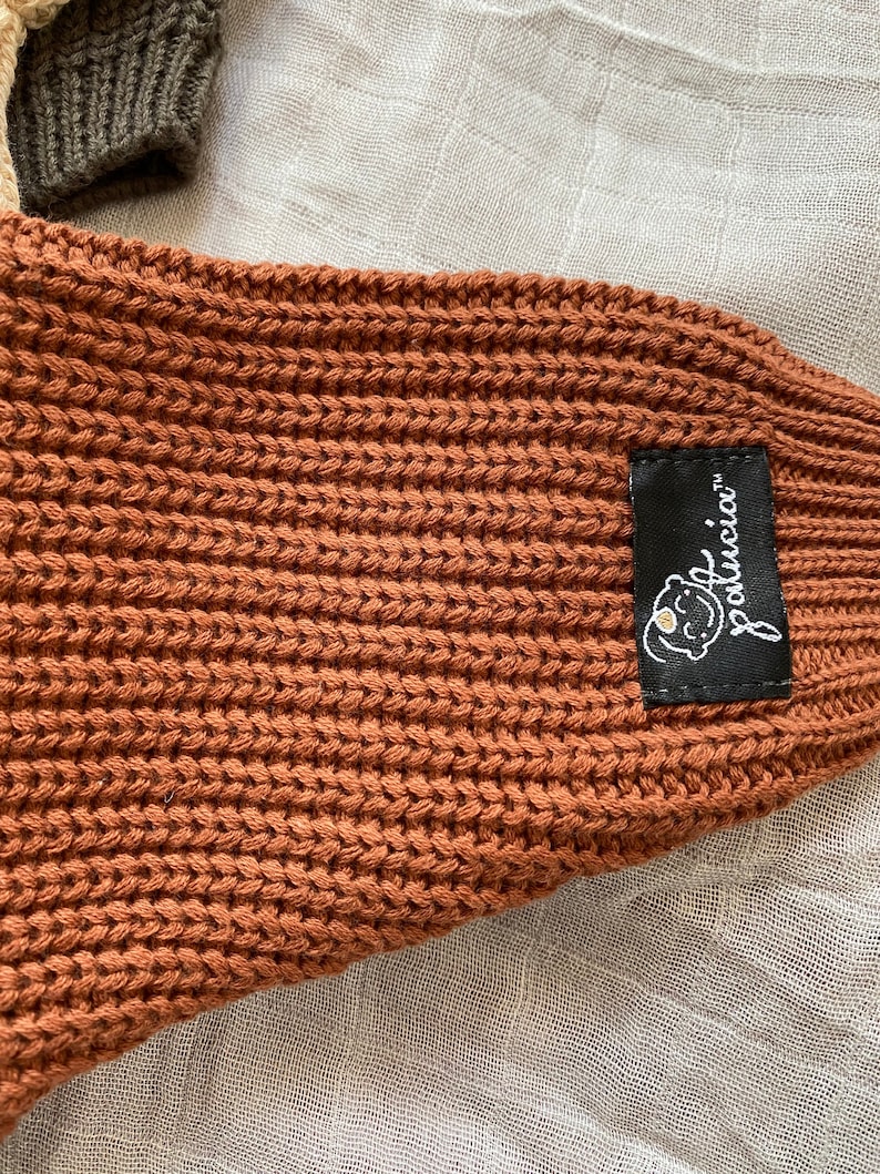 May include: A brown knitted baby blanket with a black label that says "LouLouci" with a small white flower graphic.