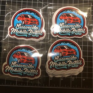 May include: A stack of white stickers with a red car and blue and white bubbles. The text on the stickers reads "Suavecito Mobile Detail".