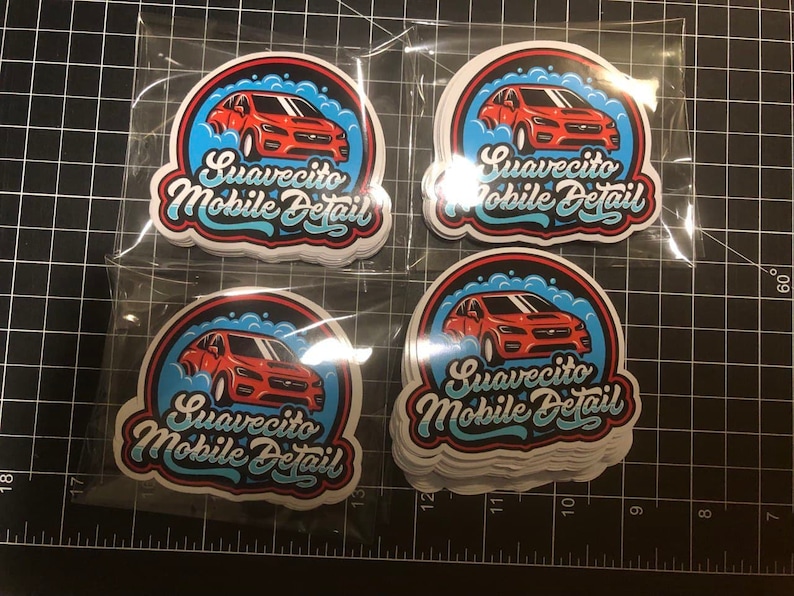 May include: A stack of white stickers with a red car and blue and white bubbles. The text on the stickers reads "Suavecito Mobile Detail".