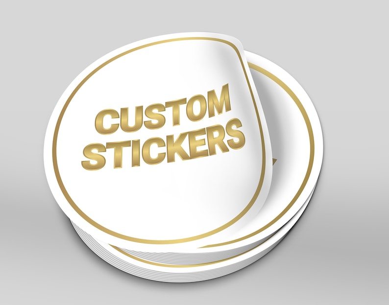 May include: A stack of round, white custom stickers with a gold border and the text "CUSTOM STICKERS" in gold lettering.