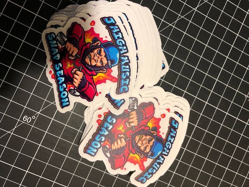 May include: A stack of white stickers with a cartoon illustration of a monkey wearing a red hoodie, blue hat, and holding a microphone. The text "5 HIGH MUSIC" and "SNAP SEASON" are on the sticker.