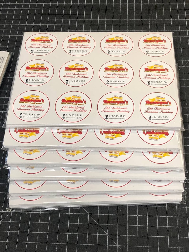 May include: A stack of white sheets of paper with red and yellow circular stickers. Each sticker has a red border and a yellow interior with a cartoon image of a train and the text "Old Fashioned Banana Pudding" and a phone number.