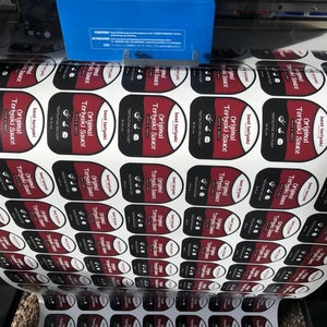 May include: A roll of white labels with red and black text that reads "Original Teriyaki Sauce" and "Best Teriyaki".