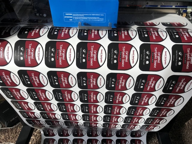 May include: A roll of white labels with red and black text that reads "Original Teriyaki Sauce" and "Best Teriyaki".