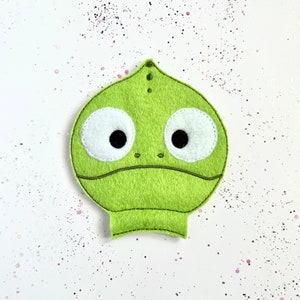 May include: A green felt chameleon puppet with large white eyes and black pupils. The puppet has a stitched mouth and a small nose.