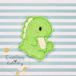 May include: Green felt dinosaur applique with white stitching. The dinosaur has a small mouth and large eyes.