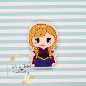 May include: Embroidered felt appliqué of a cartoon girl with long blonde hair, wearing a purple dress and a burgundy jacket. The appliqué is on a white background with blue and white stripes.