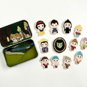 May include: A set of felt appliques featuring characters from the fairy tale Snow White. The appliques include Snow White, the Evil Queen, the Prince, the Seven Dwarfs, and the Magic Mirror. The appliques are in a tin box with a scene of Snow White's cottage.