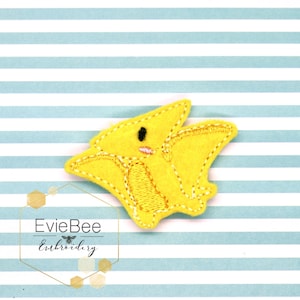 May include: Yellow felt appliqué of a cartoon pterodactyl with black eyes and a pink mouth. The appliqué is on a blue and white striped background.