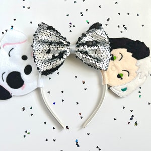 May include: A white headband with a black and silver sequined bow, a white and black dalmatian dog face on one side, and a white and black Cruella de Vil face on the other side.