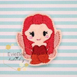 May include: Embroidered felt applique of a red-haired girl with a red and orange dress. The applique is on a light blue and white striped background.