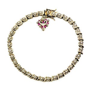 May include: A silver-toned tennis bracelet featuring a repeating S-link pattern set with small clear stones. A heart-shaped charm hangs from the clasp, decorated with a border of small pink stones surrounding a central open heart cutout design.